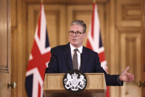 Zdjęcie przedstawia nowego premiera Wielkiej Brytanii Keira Starmera, który przemawia na konferencji prasowej, za nim stoją dwie flagi Wielkiej Brytanii